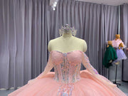 Pink quinceañera dress with corset bodice, illusion sleeves, and princess silhouette skirt.