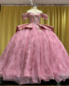 Sparkling pink quinceañera ball gown with off-shoulder sleeves, satin peplum, and glitter tulle skirt.